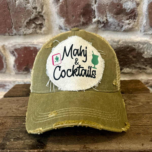 Mahj & Cocktails hat by BohoGroove featuring black Mahj & Cocktails lettering with a green cocktail graphic and Mahjong tile graphic on an off-white distressed patch on an olive vintage distressed snapback trucker hat.