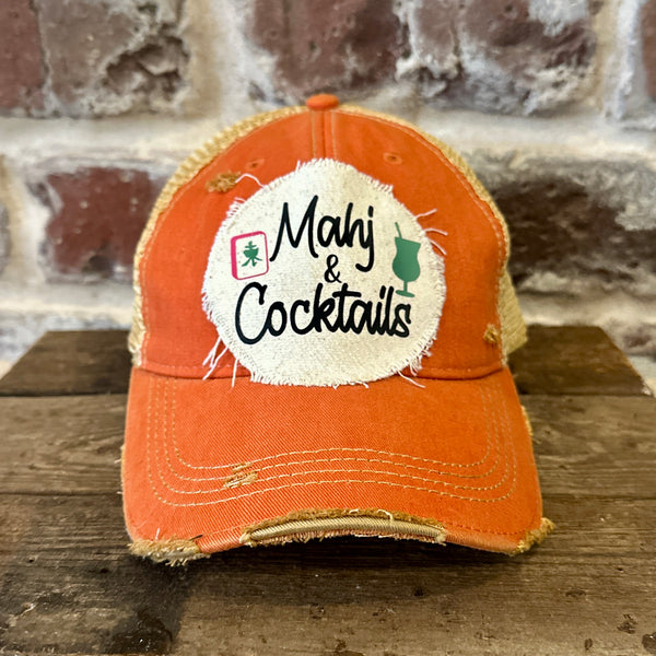 Mahj & Cocktails hat by BohoGroove featuring black Mahj & Cocktails lettering with a green cocktail graphic and Mahjong tile graphic on an off-white distressed patch on an orange vintage distressed snapback trucker hat.