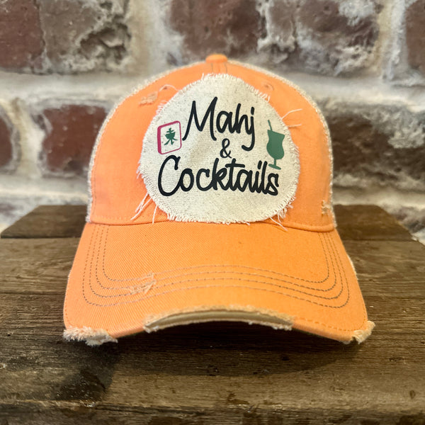 Mahj & Cocktails hat by BohoGroove featuring black Mahj & Cocktails lettering with a green cocktail graphic and Mahjong tile graphic on an off-white distressed patch on a sherbet vintage distressed snapback trucker hat.