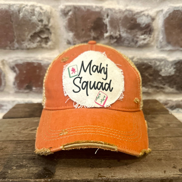 Mahj Squad hat by BohoGroove featuring black Mahj Squad lettering with Mahjong tile graphics on an off-white distressed patch on an orange vintage distressed snapback trucker hat.