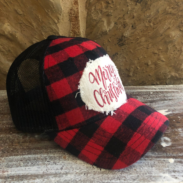 Left side view of the Merry Christmas hat by BohoGroove featuring red glitter Merry Christmas script lettering on a distressed off-white patch on a red and black buffalo plaid snapback trucker hat with black mesh back.