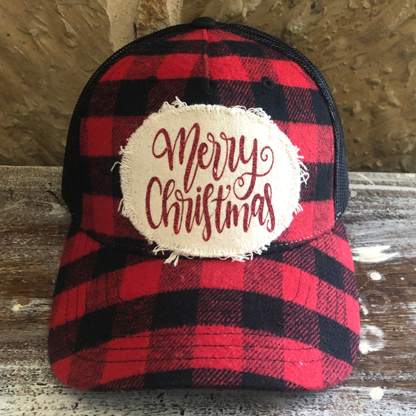 Merry Christmas hat by BohoGroove with red glitter Merry Christmas script lettering on a distressed off-white patch on a red and black buffalo plaid snapback trucker hat.