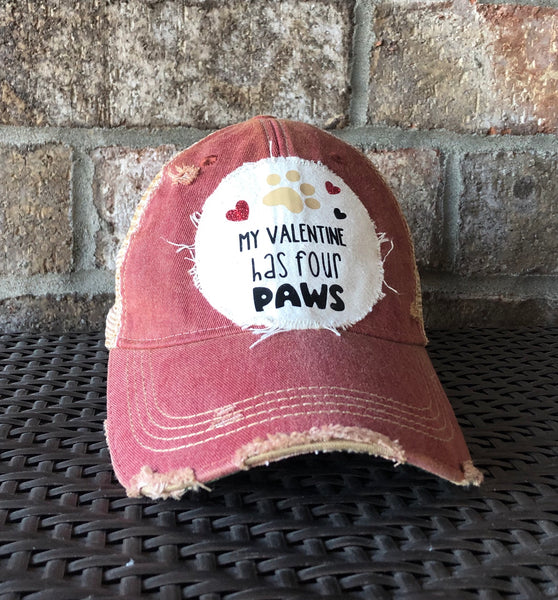 My Valentine Has Four Paws hat by BohoGroove with black My Valentine Has Four Paws lettering, tan paw print graphic, and red and black heart graphics on a distressed off-white patch on a brick red vintage distressed snapback.