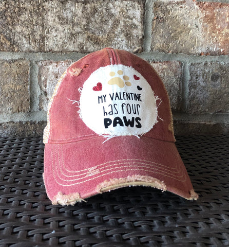 Red distressed cap with 'My Valentine Has Four Paws' text on a stone wall background