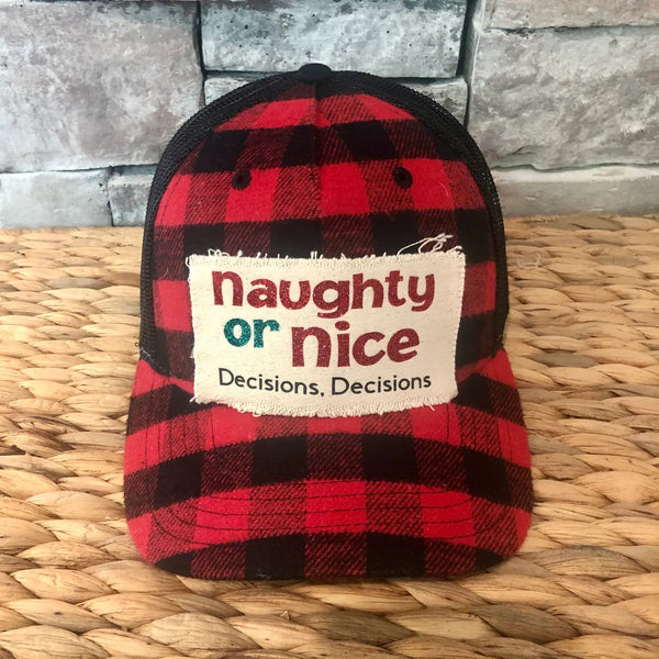 Naughty or Nice hat by BohoGroove with red and green Naughty or Nice lettering and Decisions, Decisions wording on a distressed off-white patch on a red and black buffalo plaid snapback trucker hat.