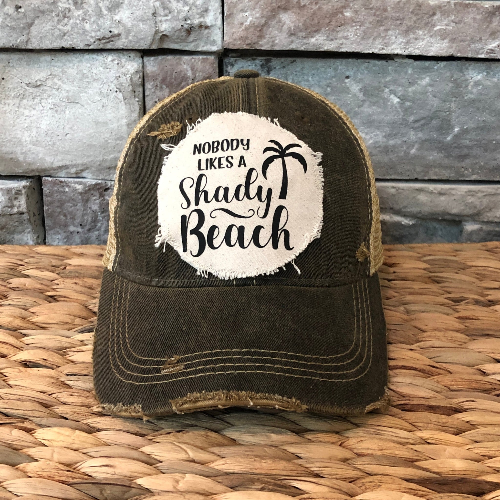 Vintage-style cap with 'Nobody Likes a Shady Beach' text on a stone wall background