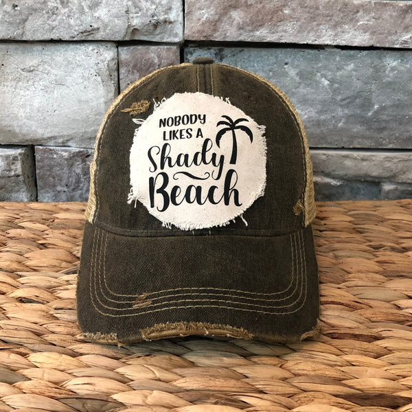 Vintage-style cap with 'Nobody Likes a Shady Beach' text on a stone wall background