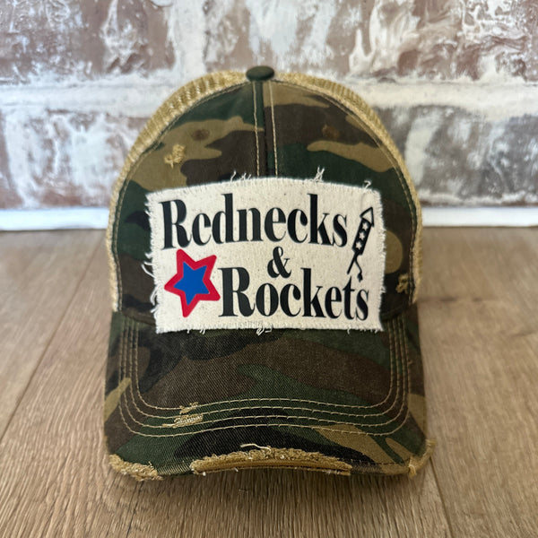Rednecks And Rockets hat by BohoGroove with black lettering, red and blue star graphic, and firework rocket graphic on distressed off-white patch on camo vintage distressed snapback.