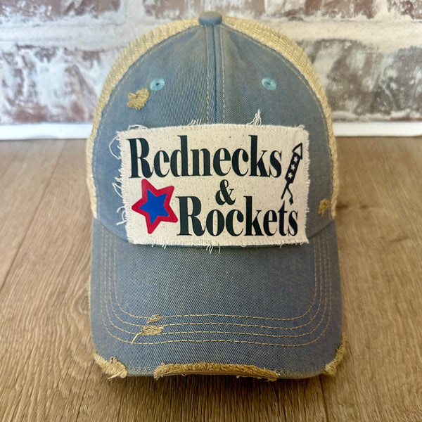 Rednecks And Rockets hat by BohoGroove with black lettering, red and blue star graphic, and firework rocket graphic on distressed off-white patch on light blue vintage distressed snapback.