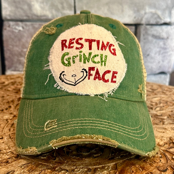 Resting Grinch Face hat by BohoGroove with red and green Resting Grinch Face lettering and Grinch-inspired face graphic on a distressed off-white custom patch on a green vintage distressed snapback.