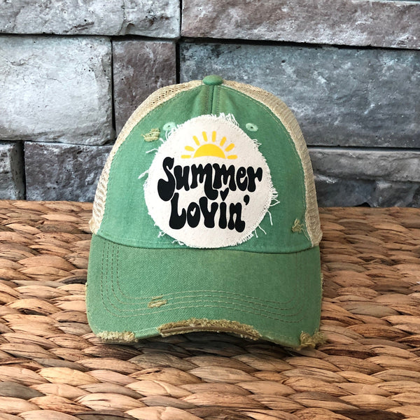 Green cap with a summer lovin logo on a woven surface and stone wall background