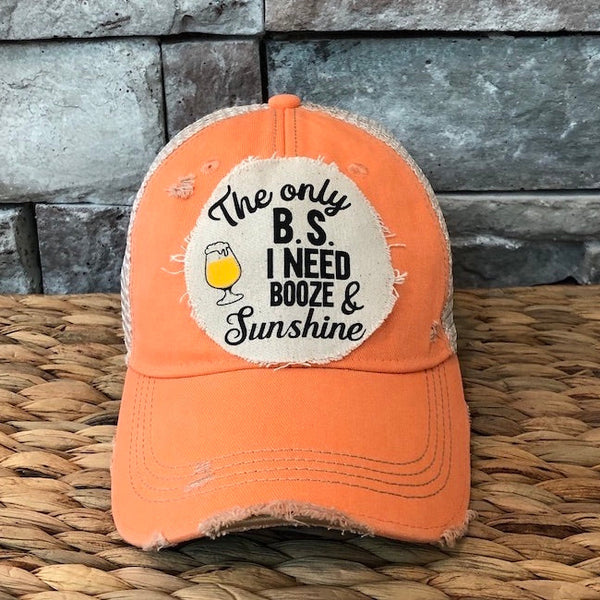 Orange cap with a patch that reads 'The only B.S. I need is booze & sunshine' on a stone wall background.