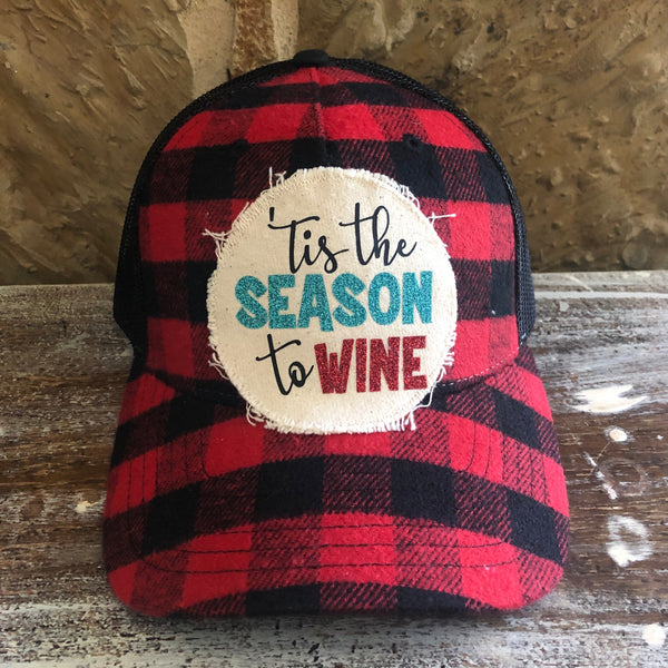 Tis the Season to Wine hat by BohoGroove with black Tis the wording, teal glitter Season lettering, and red glitter Wine lettering on a distressed off-white patch on a red and black buffalo plaid snapback trucker hat.