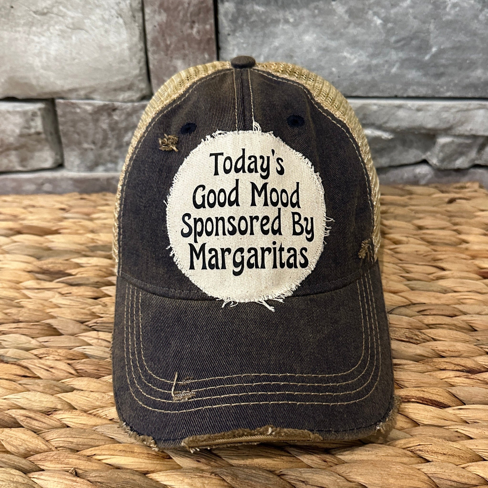 Black and brown cap with 'Today's Good Mood Sponsored By Margaritas' text on a woven surface.