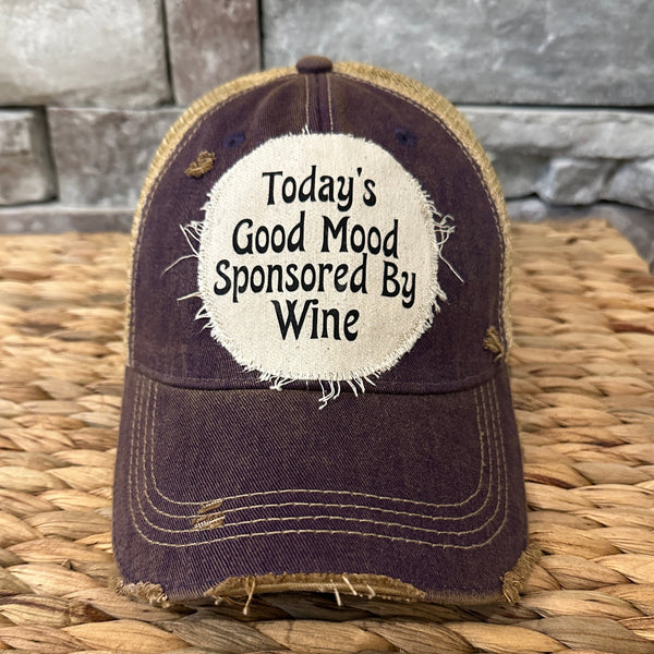purple Cap with 'Today's Good Mood Sponsored By Wine' text on a woven surface and stone wall background
