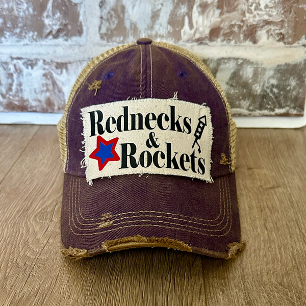 Rednecks And Rockets hat by BohoGroove with black lettering, red and blue star graphic, and firework rocket graphic on distressed off-white patch on purple vintage distressed snapback.
