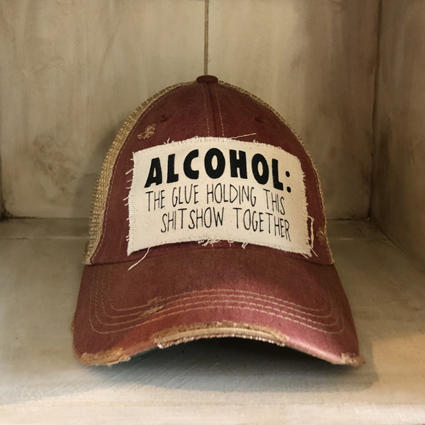 Alcohol: The Glue Holding This Shitshow Together hat by BohoGroove with black lettering on a distressed off-white patch on a brick red vintage distressed snapback trucker hat.