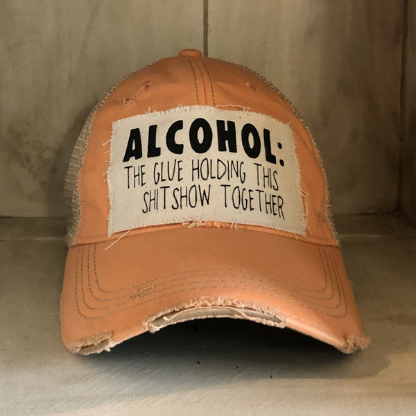 Alcohol: The Glue Holding This Shitshow Together hat by BohoGroove with black lettering on a distressed off-white patch on a sherbet vintage distressed snapback trucker hat.