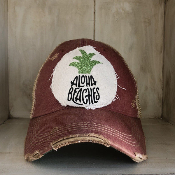 Aloha Beaches hat by BohoGroove with black Aloha Beaches lettering and green pineapple graphic on distressed off-white patch and brick red vintage distressed snapback.