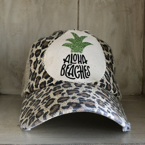 Aloha Beaches hat by BohoGroove with black Aloha Beaches lettering and green pineapple graphic on distressed off-white patch and leopard vintage distressed snapback.