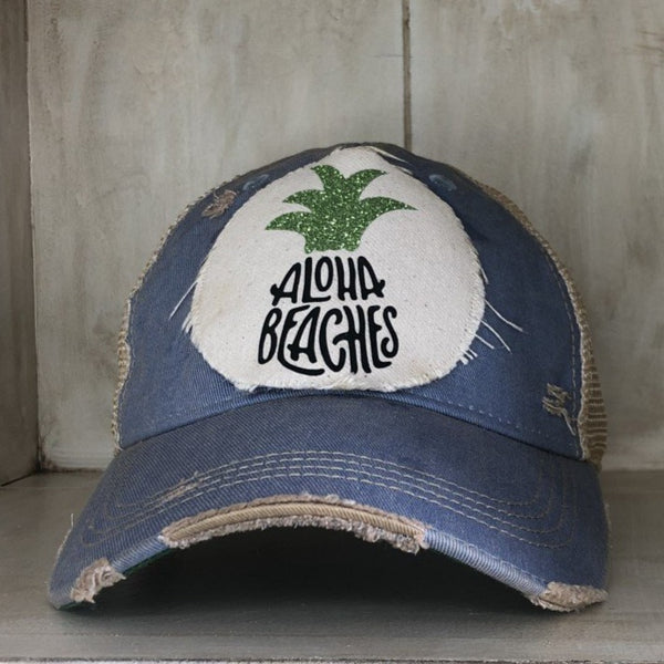 Aloha Beaches hat by BohoGroove with black Aloha Beaches lettering and green pineapple graphic on distressed off-white patch and light blue vintage distressed snapback.