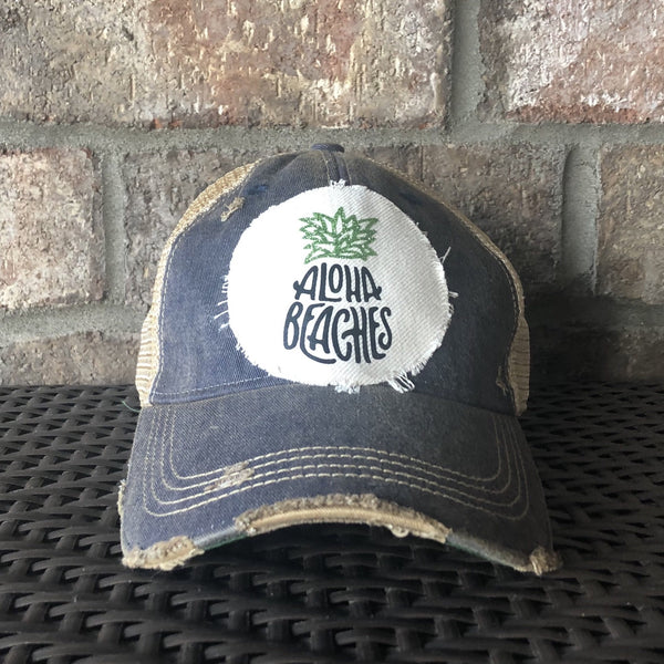Aloha Beaches hat by BohoGroove with black Aloha Beaches lettering and green pineapple graphic on distressed off-white patch and navy blue vintage distressed snapback.