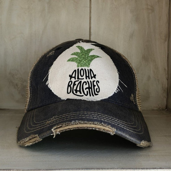 Aloha Beaches hat by BohoGroove with black Aloha Beaches lettering and green pineapple graphic on distressed off-white patch and navy blue vintage distressed snapback.