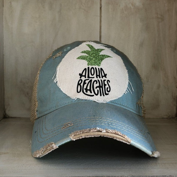 Aloha Beaches hat by BohoGroove with black Aloha Beaches lettering and green pineapple graphic on distressed off-white patch and ocean blue vintage distressed snapback.