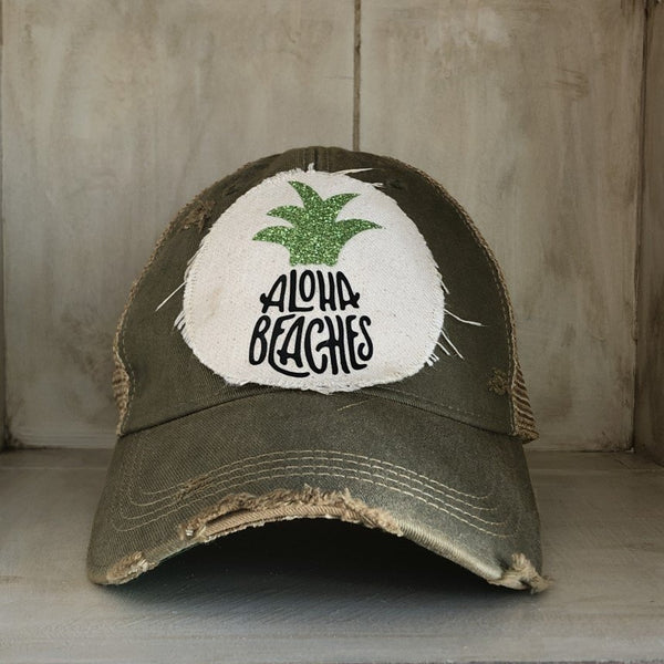 Aloha Beaches hat by BohoGroove with black Aloha Beaches lettering and green pineapple graphic on distressed off-white patch and olive vintage distressed snapback.
