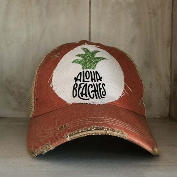 Aloha Beaches hat by BohoGroove with black Aloha Beaches lettering and green pineapple graphic on distressed off-white patch and orange vintage distressed snapback.