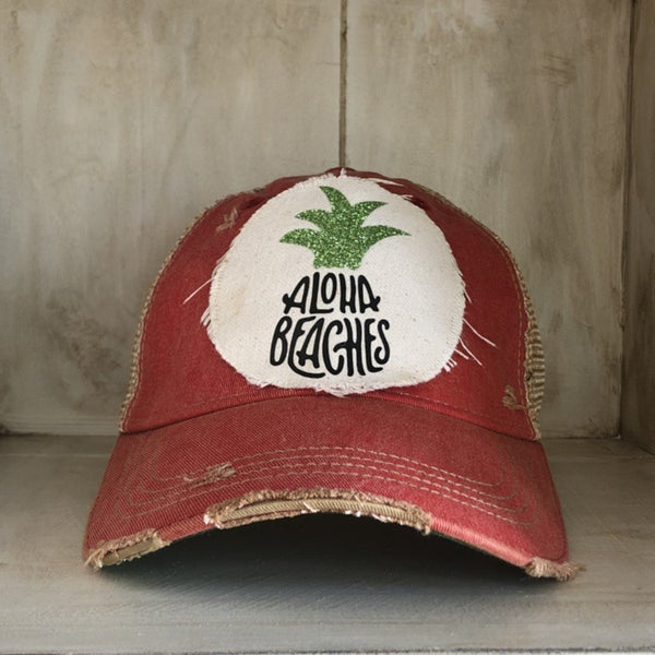 Aloha Beaches hat by BohoGroove with black Aloha Beaches lettering and green pineapple graphic on distressed off-white patch and red vintage distressed snapback.