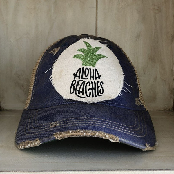 Aloha Beaches hat by BohoGroove with black Aloha Beaches lettering and green pineapple graphic on distressed off-white patch and royal blue vintage distressed snapback.