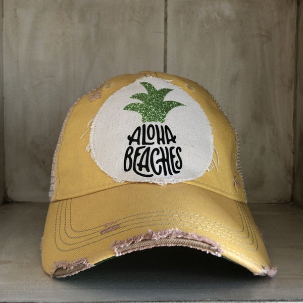 Aloha Beaches hat by BohoGroove with black Aloha Beaches lettering and green pineapple graphic on distressed off-white patch and yellow vintage distressed snapback.