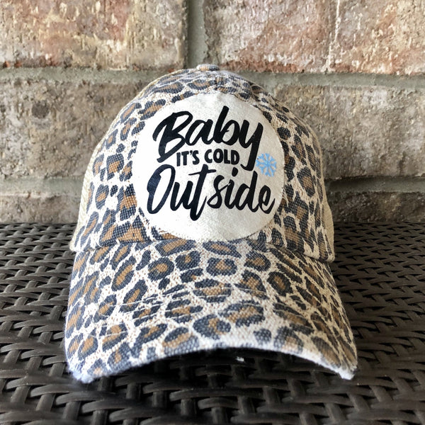 Baby It's Cold Outside hat by BohoGroove with black script lettering and a blue snowflake graphic on a distressed off-white custom patch on a leopard vintage distressed snapback.