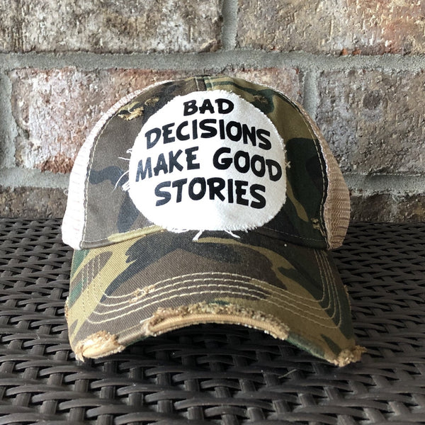 Bad Decisions Make Good Stories hat by BohoGroove with black Bad Decisions Make Good Stories lettering on a distressed off-white patch on a camo vintage distressed snapback trucker hat.