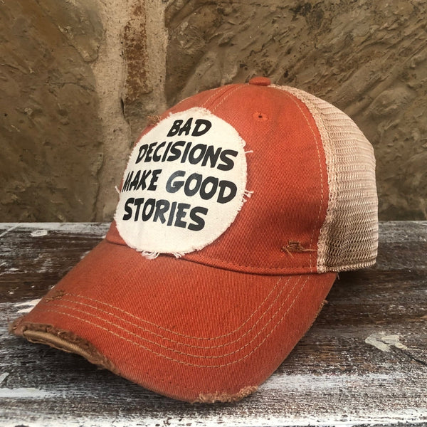 Right side view of Bad Decisions Make Good Stories hat by BohoGroove with black Bad Decisions Make Good Stories lettering on a distressed off-white patch on an orange vintage distressed snapback trucker hat.