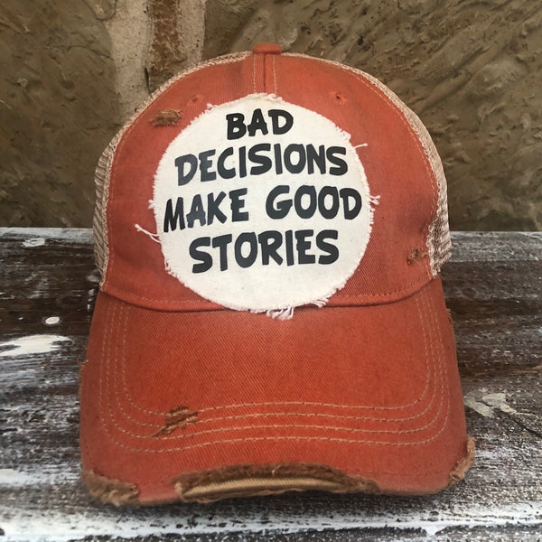 Bad Decisions Make Good Stories hat by BohoGroove with black Bad Decisions Make Good Stories lettering on a distressed off-white patch on an orange vintage distressed snapback trucker hat.