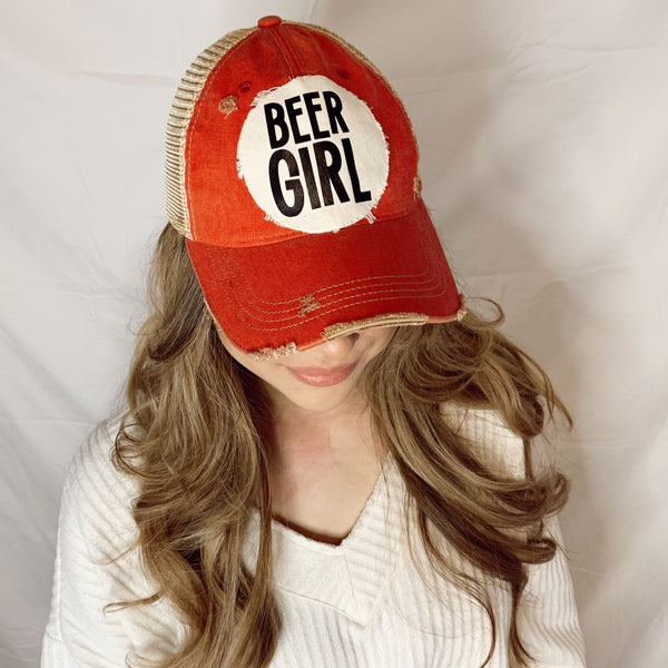 Close-up of a woman wearing a Beer Girl hat by BohoGroove featuring black Beer Girl lettering on a distressed off-white patch on a brick red vintage distressed snapback trucker hat.