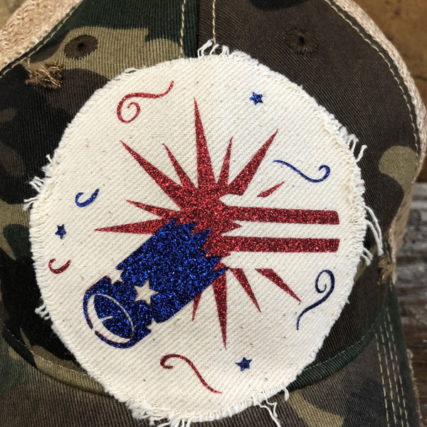 Firework hat by BohoGroove featuring blue glitter firework cannon, red firework burst, and patriotic stars on distressed off-white patch and camo vintage distressed snapback