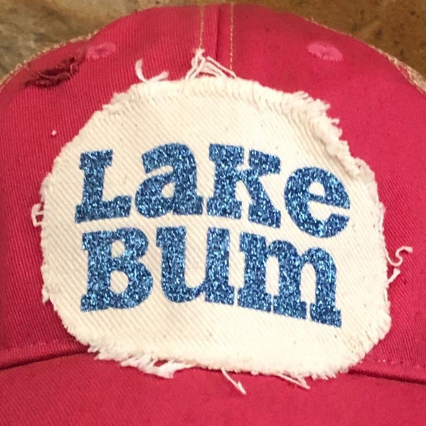 Close up picture Lake Bum hat by BohoGroove with blue glitter Lake Bum lettering on distressed off-white patch on a pink vintage distressed snapback.