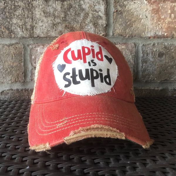 Cupid Is Stupid hat by BohoGroove with red and black Cupid Is Stupid lettering and black heart graphics on a distressed off-white patch on a red vintage distressed snapback trucker hat.