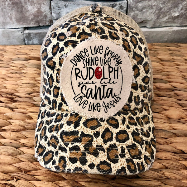 Dance Like Frosty Shine Like Rudolph Give Like Santa Love Like Jesus hat by BohoGroove with red and green lettering and Christmas phrase on a distressed off-white patch on a leopard vintage distressed snapback.