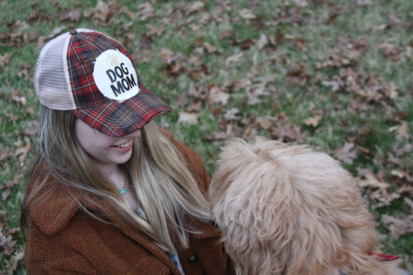 A woman wearing a BohoGroove Dog Mom snapback hat enjoys time outdoors with her dog on a fall day. The lifestyle image showcases the vintage distressed Dog Mom design and highlights the special bond between dog moms and their four-legged best friends.