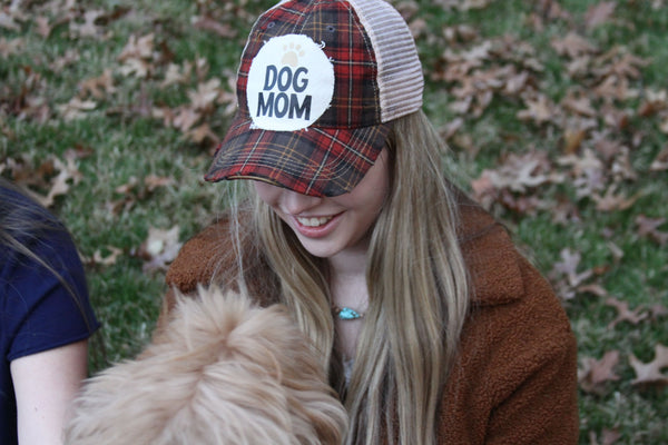 A woman wearing a BohoGroove Dog Mom snapback hat enjoys time outdoors with her dog on a fall day. The lifestyle image showcases the vintage distressed Dog Mom design and highlights the special bond between dog moms and their four-legged best friends.