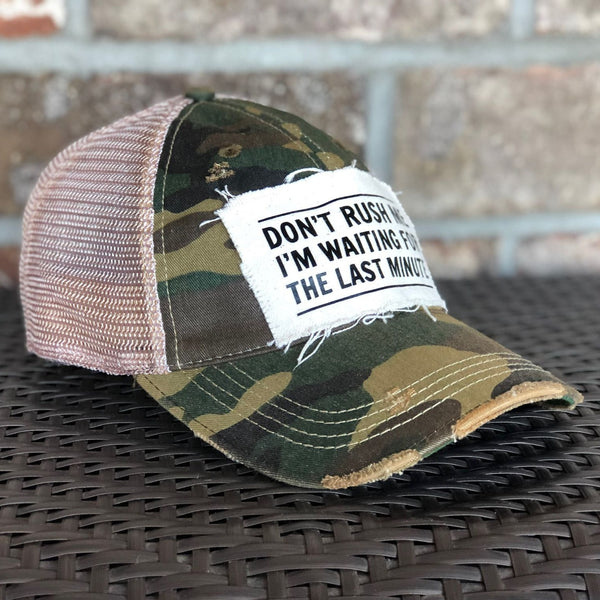 Left side view of the Don't Rush Me I'm Waiting for the Last Minute hat by BohoGroove with black lettering on a distressed off-white patch on a camo vintage distressed snapback trucker hat.