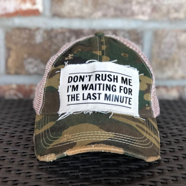 Don't Rush Me I'm Waiting for the Last Minute hat by BohoGroove with black lettering on a distressed off-white patch on a camo vintage distressed snapback trucker hat.