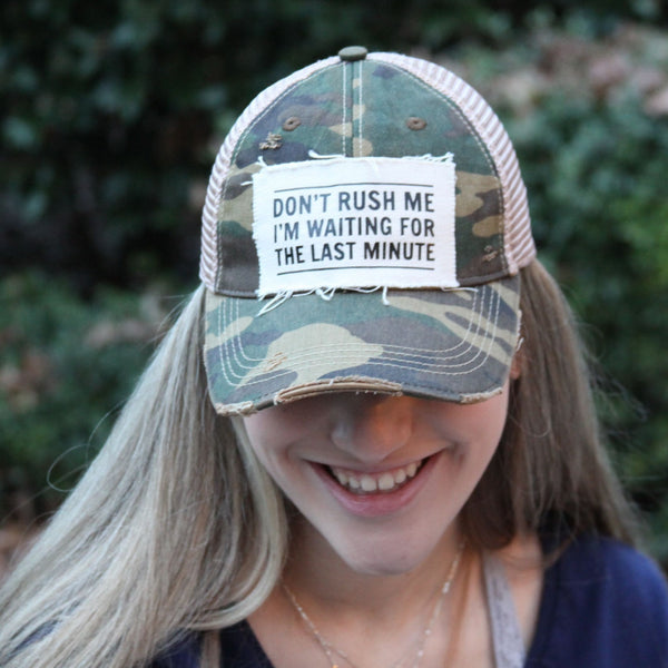 Woman wearing the Don't Rush Me I'm Waiting for the Last Minute hat by BohoGroove with black lettering on a distressed off-white patch on a camo vintage distressed snapback trucker hat.