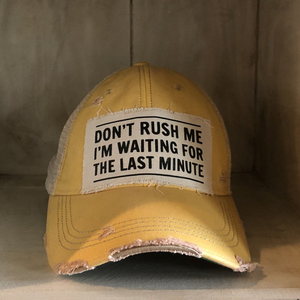 Don't Rush Me I'm Waiting for the Last Minute hat by BohoGroove with black lettering on a distressed off-white patch on a yellow vintage distressed snapback trucker hat.
