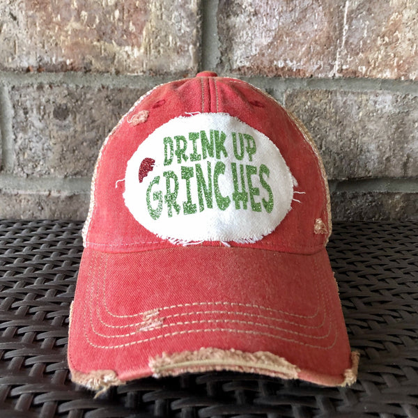 Drink Up Grinches hat by BohoGroove with glitter green Drink Up Grinches lettering and a red Santa hat graphic on a distressed off-white custom patch on a red vintage distressed snapback.
