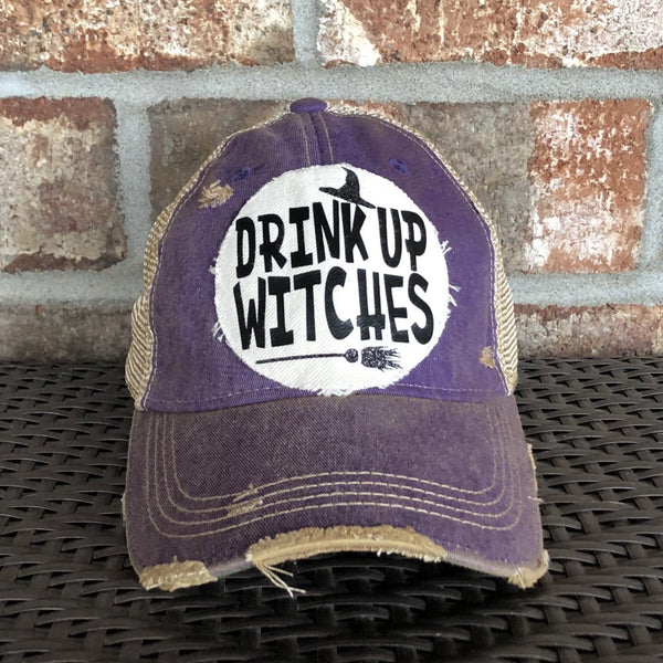 Drink Up Witches hat by BohoGroove with black Drink Up Witches lettering, witch hat graphic and broom graphic on a distressed off-white patch on a purple vintage distressed snapback.
